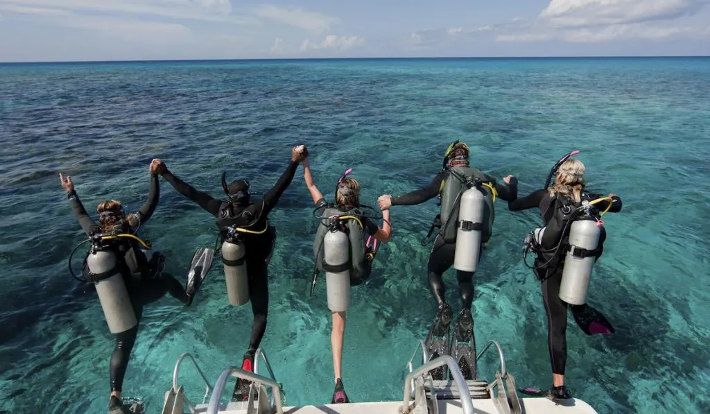 group of 5 friends jumping in the ocean to scuba dive
