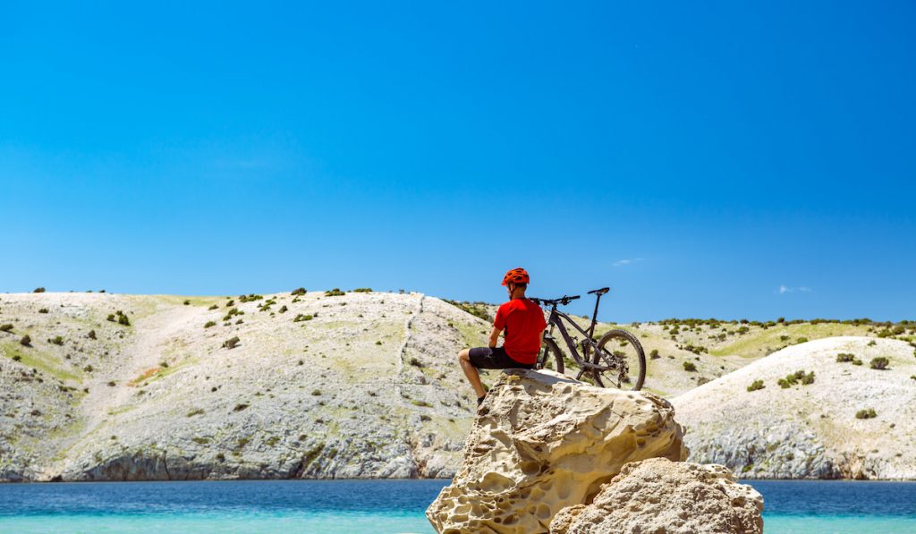 mountain biker sitting on top of rock looking at beach