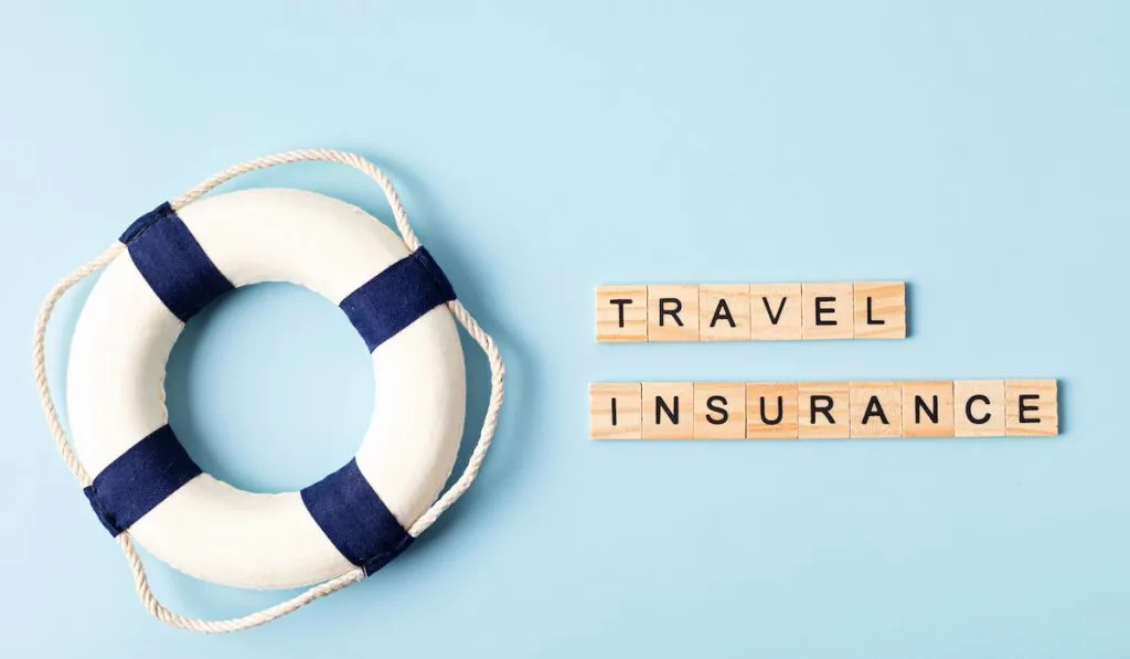 Lifebuoy over blue background with travel insurance wooden letters